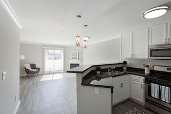 An empty kitchen and living room with white cabinets and black counter tops